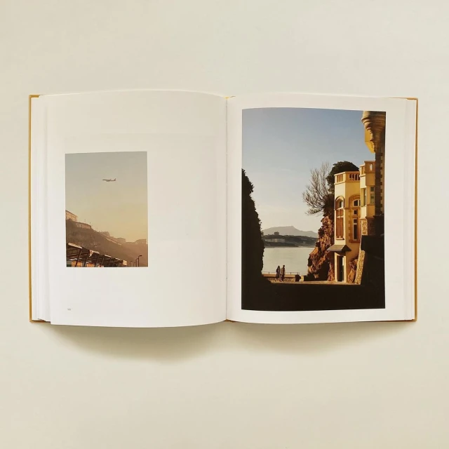 Open book displaying two landscape photographs, one with an airplane over buildings and the other with a building on a coast.