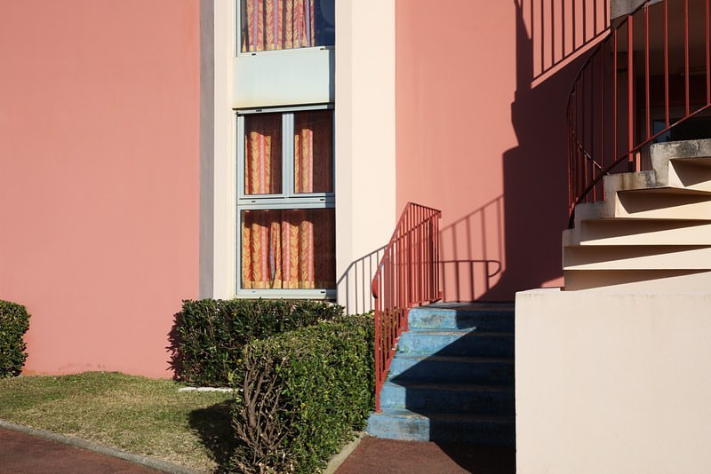 Exterior architectural view of a pink building with blue stairs and a red railing under natural sunlight in Paris.