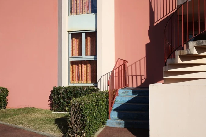 Exterior architectural view of a pink building with blue stairs and a red railing under natural sunlight in Paris.