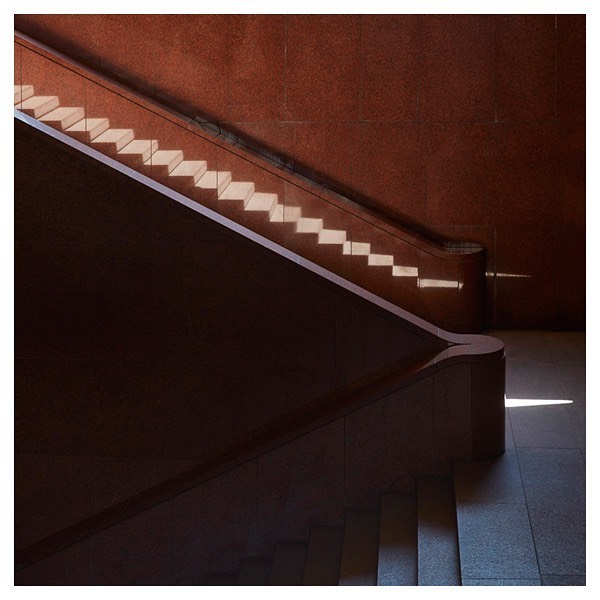 Stairway with geometric shadows cast by natural light on the steps, adjacent wall, and the handrail inside a building.