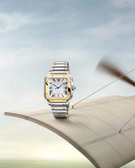 Luxury wristwatch with gold and silver band on the wing of an antique airplane against a blue sky backdrop, studio product shot.