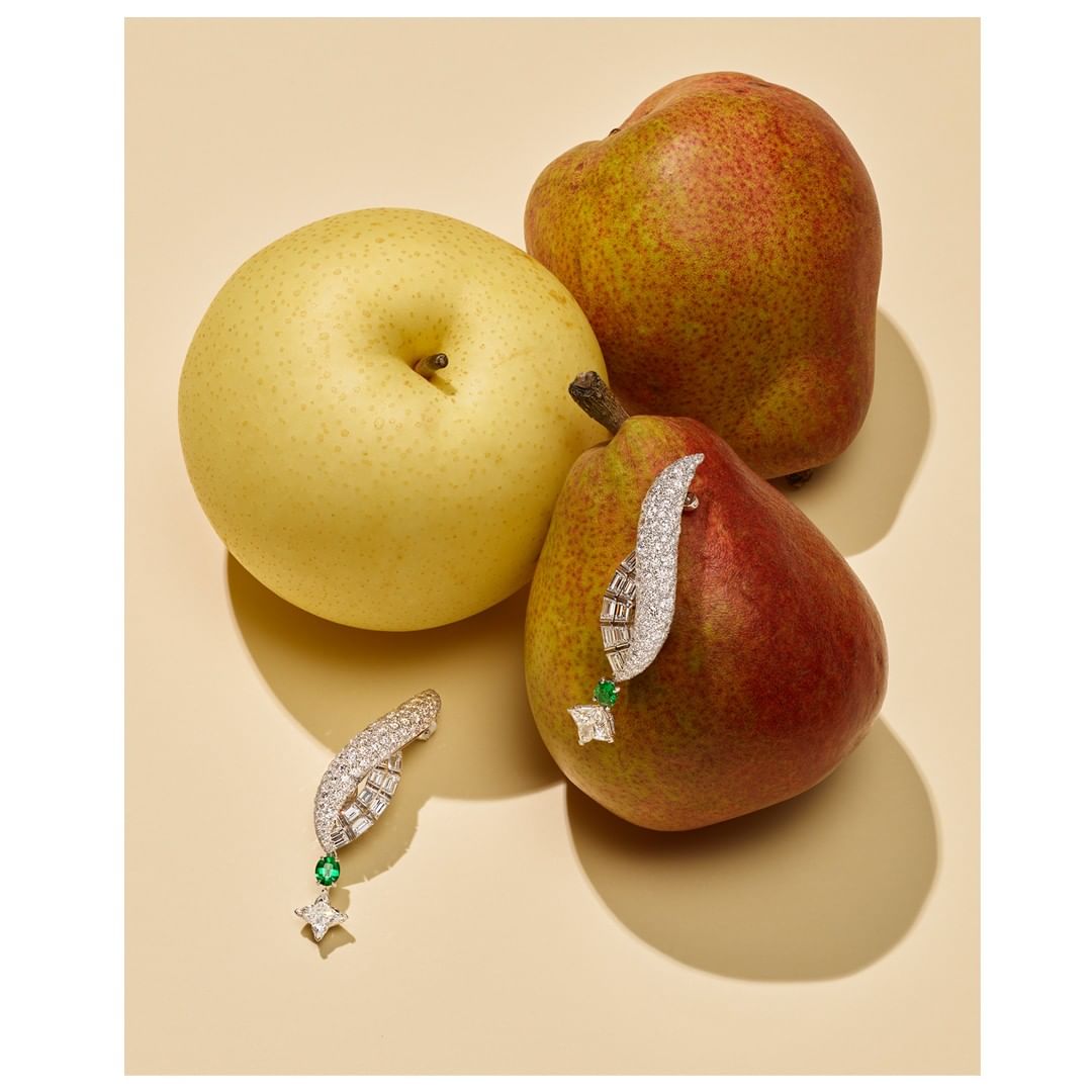 Still life featuring two jewelry earrings on red and yellow pears on a beige surface, jewellery product photography.