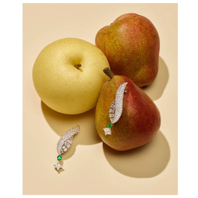 Still life featuring two jewelry earrings on red and yellow pears on a beige surface, jewellery product photography.