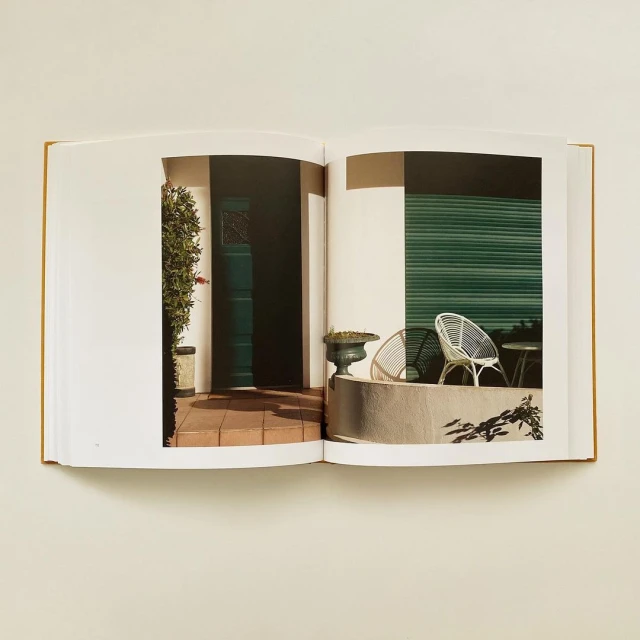 Open book shows a photo of an exterior home entrance with a dark door, planters, a low concrete wall, and chairs on a tile surface.