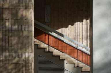 Architectural interior view of a tiled staircase with diagonal sunlight casting geometric shadows by Roberto Badin in Paris.