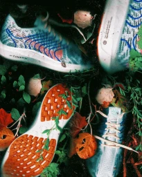 Multiple running shoes nestled amongst damp green leaves, twigs, and fallen autumn foliage in a dark forest setting
