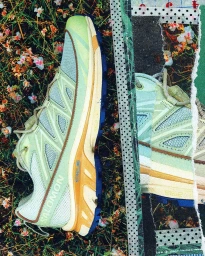 Salomon trail running sneaker featuring pale green mesh and blue accents layered over a torn paper collage background.