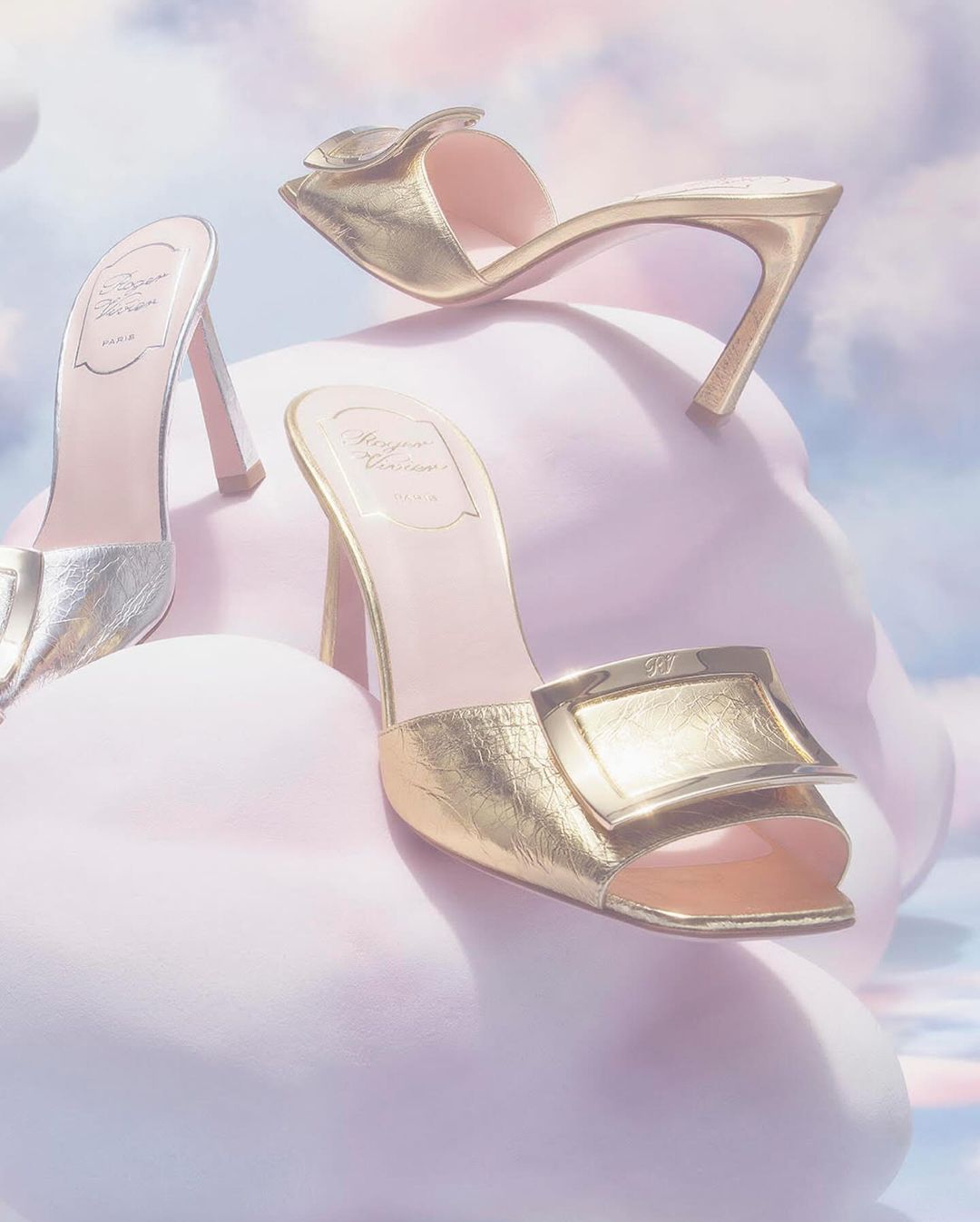 Three luxury gold and silver high-heeled shoes are displayed against a dreamy soft-focus cloudy background, fashion editorial.