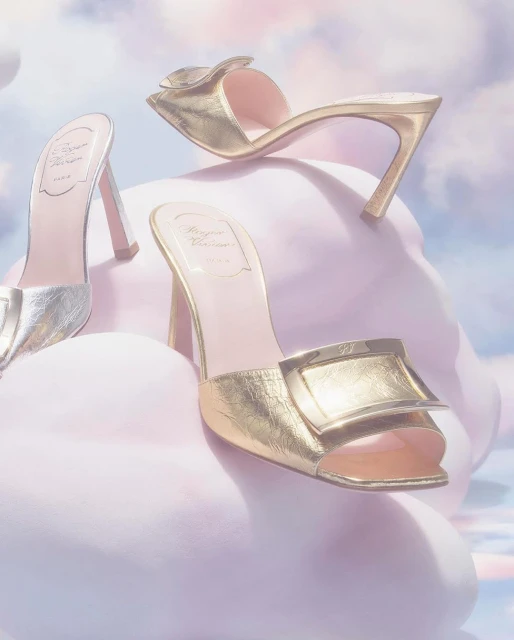 Three luxury gold and silver high-heeled shoes are displayed against a dreamy soft-focus cloudy background, fashion editorial.