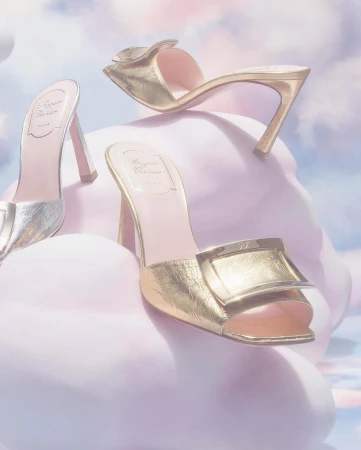 Three luxury gold and silver high-heeled shoes are displayed against a dreamy soft-focus cloudy background, fashion editorial.