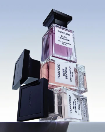 Stacked Tom Ford fragrance bottles with black caps against a pale gradient background