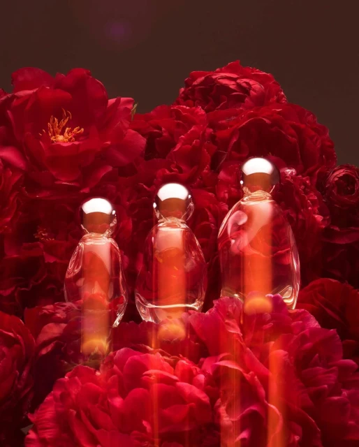 Three perfume bottles with silver caps arranged among vibrant red peony flowers, creating an elegant and eye-catching beauty product still life.