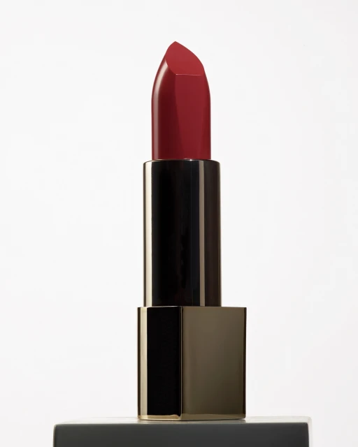 Close-up studio shot of a dark red lipstick with a black and gold tube, reflecting light against a solid white background.
