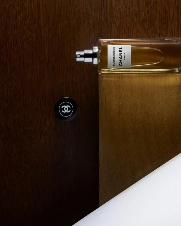 A rectangular amber glass perfume bottle with silver spray nozzle positioned horizontally against a dark wood panel surface.