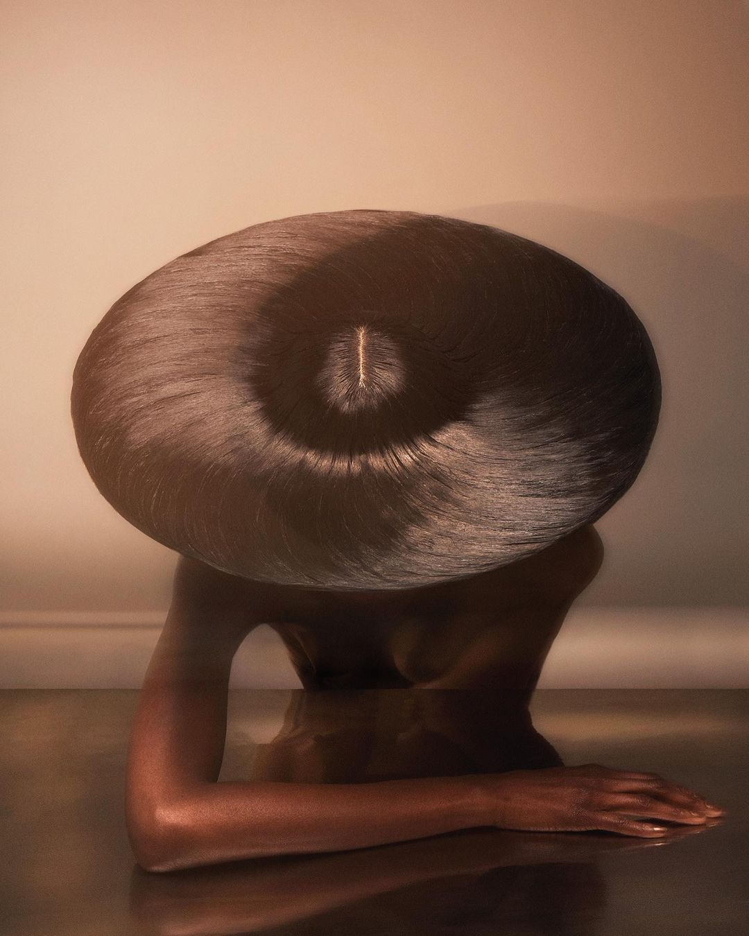 Stylish portrait of a dark-skinned woman featuring an exaggerated black, spiral-shaped hairstyle and reflective surface.