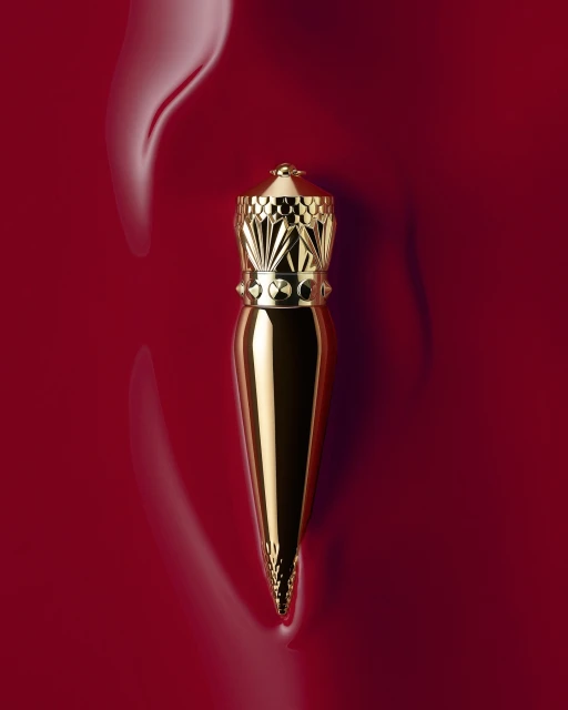 High-angle studio shot of a gold lipstick tube with a decorative crown-shaped cap on a glossy, deep red background.