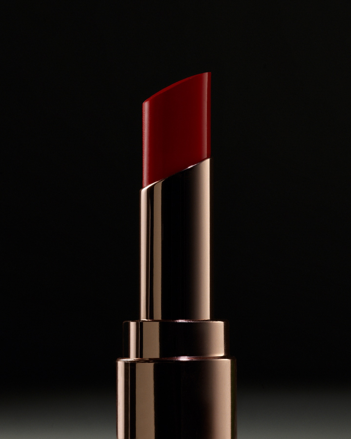 Close-up product shot of a shiny red lipstick in a reflective metallic gold tube against a dark background