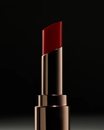 Close-up product shot of a shiny red lipstick in a reflective metallic gold tube against a dark background