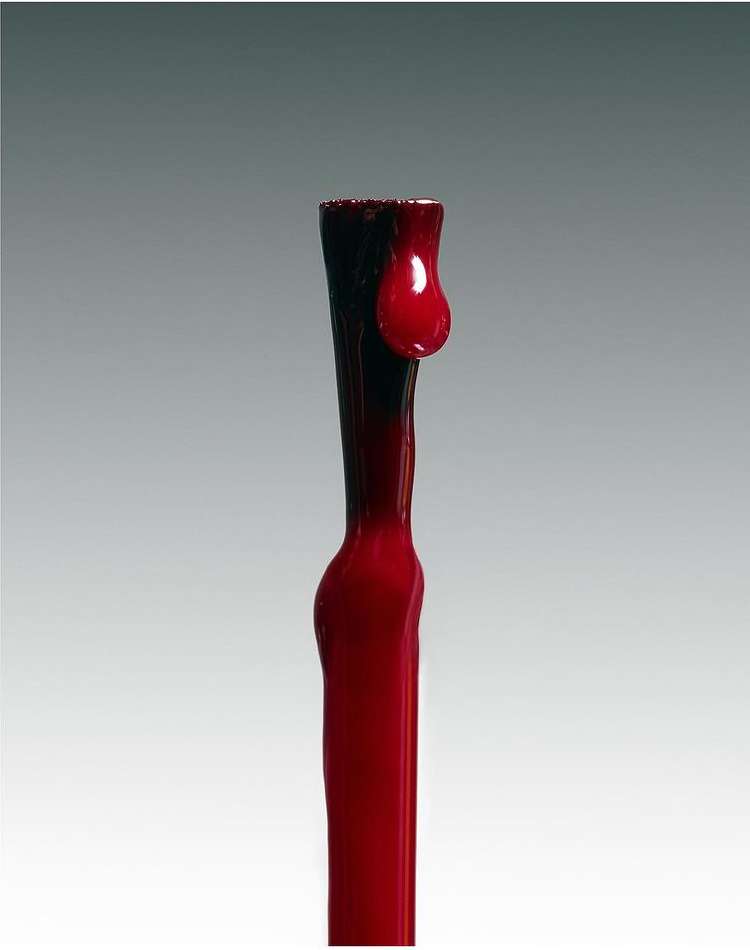 A red liquid dripping down a dark rod, with a droplet suspended. The backdrop is a simple gray gradient.