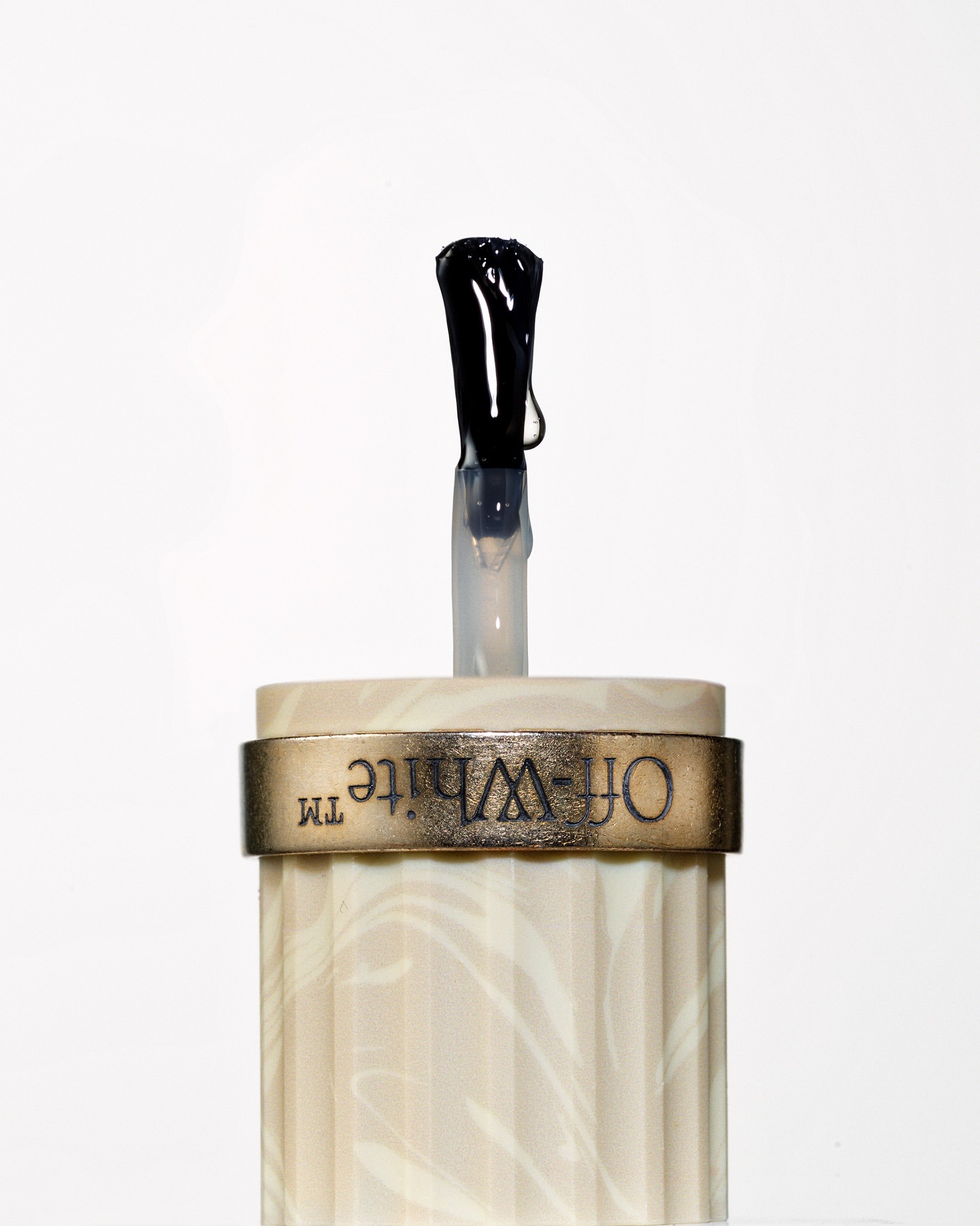 Close-up studio shot of an Off-White nail polish applicator with a black brush, set against a clean white backdrop, product presentation.