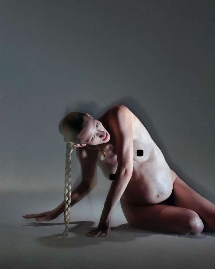 Woman poses in a photo studio with her body angled and braided hair; gray background and low-key lighting.