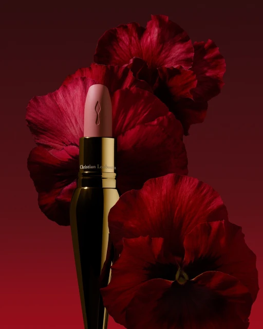 Close-up studio shot of light pink Christian Louboutin lipstick tube with a gold base against dark red hibiscus flowers.