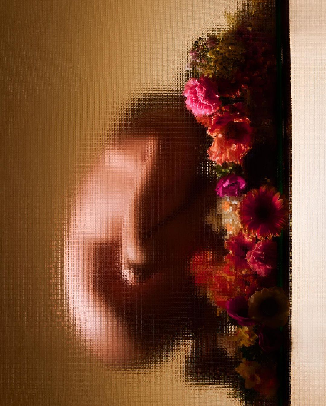 Blurred figure of a person behind textured glass with bright pink, orange, and yellow flowers on the right side of the frame.