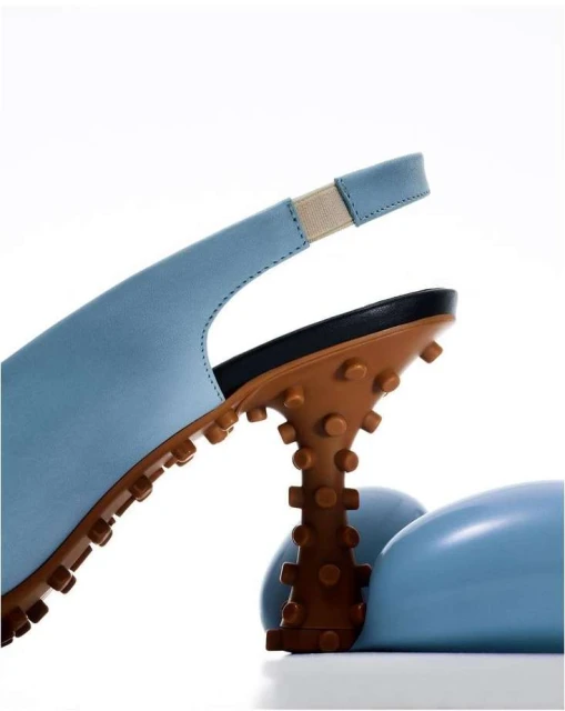 Close-up of a light blue slingback shoe with a distinctive brown, textured heel and sole, set against a clean white background.