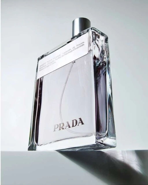 Product shot of a rectangular glass bottle of Prada fragrance with a silver cap, against a neutral white background with soft lighting.