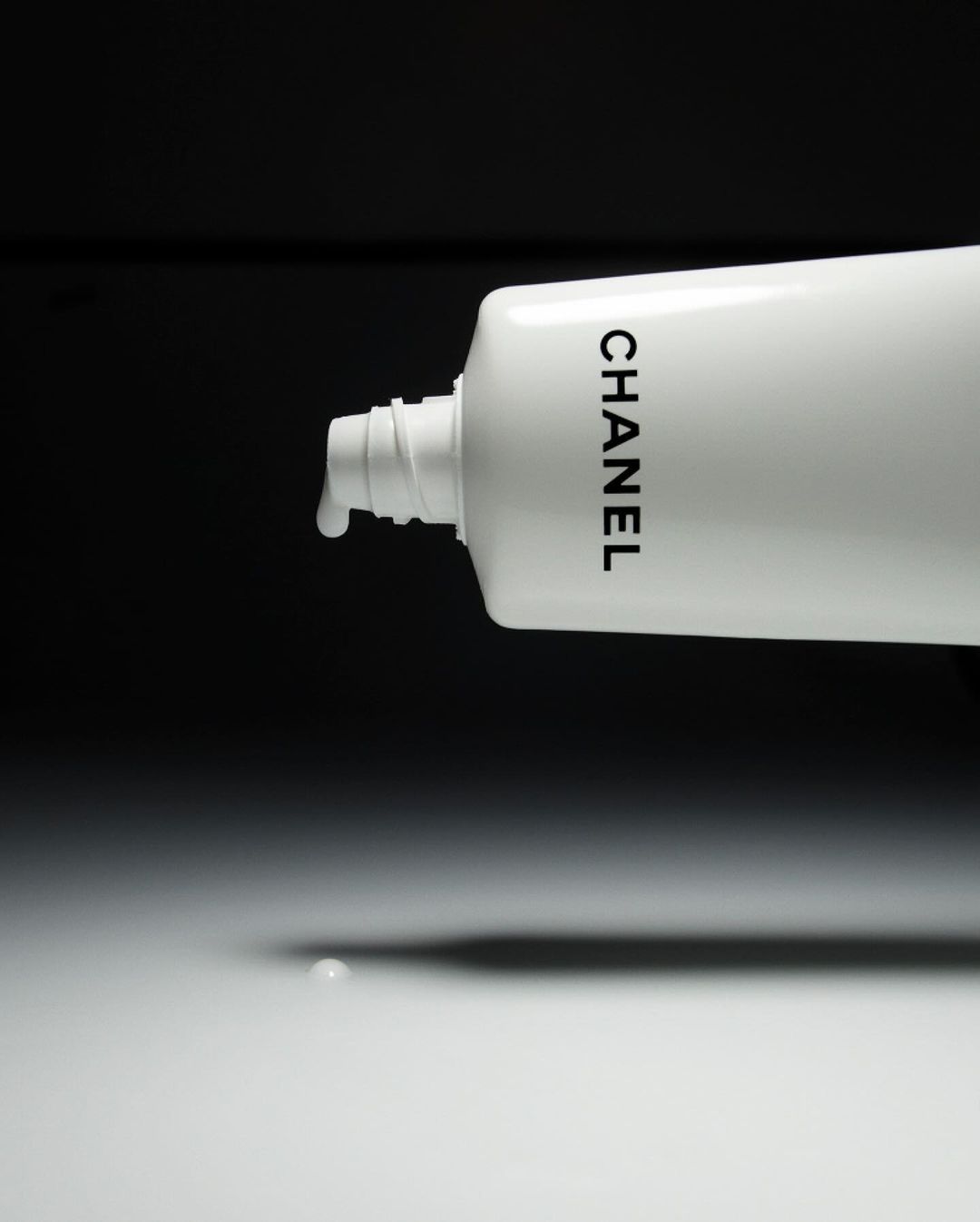 White Chanel tube with liquid dispensing, set against a contrasting black backdrop, creating a minimalistic beauty still-life product shot.