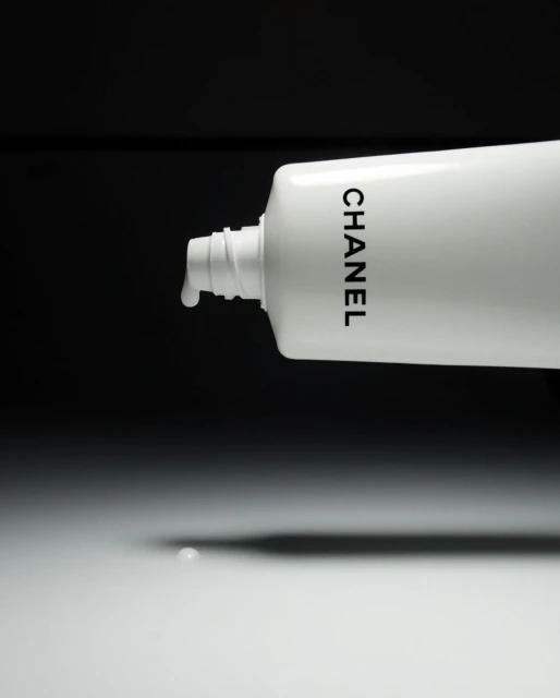White Chanel tube with liquid dispensing, set against a contrasting black backdrop, creating a minimalistic beauty still-life product shot.