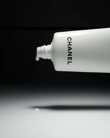White Chanel tube with liquid dispensing, set against a contrasting black backdrop, creating a minimalistic beauty still-life product shot.