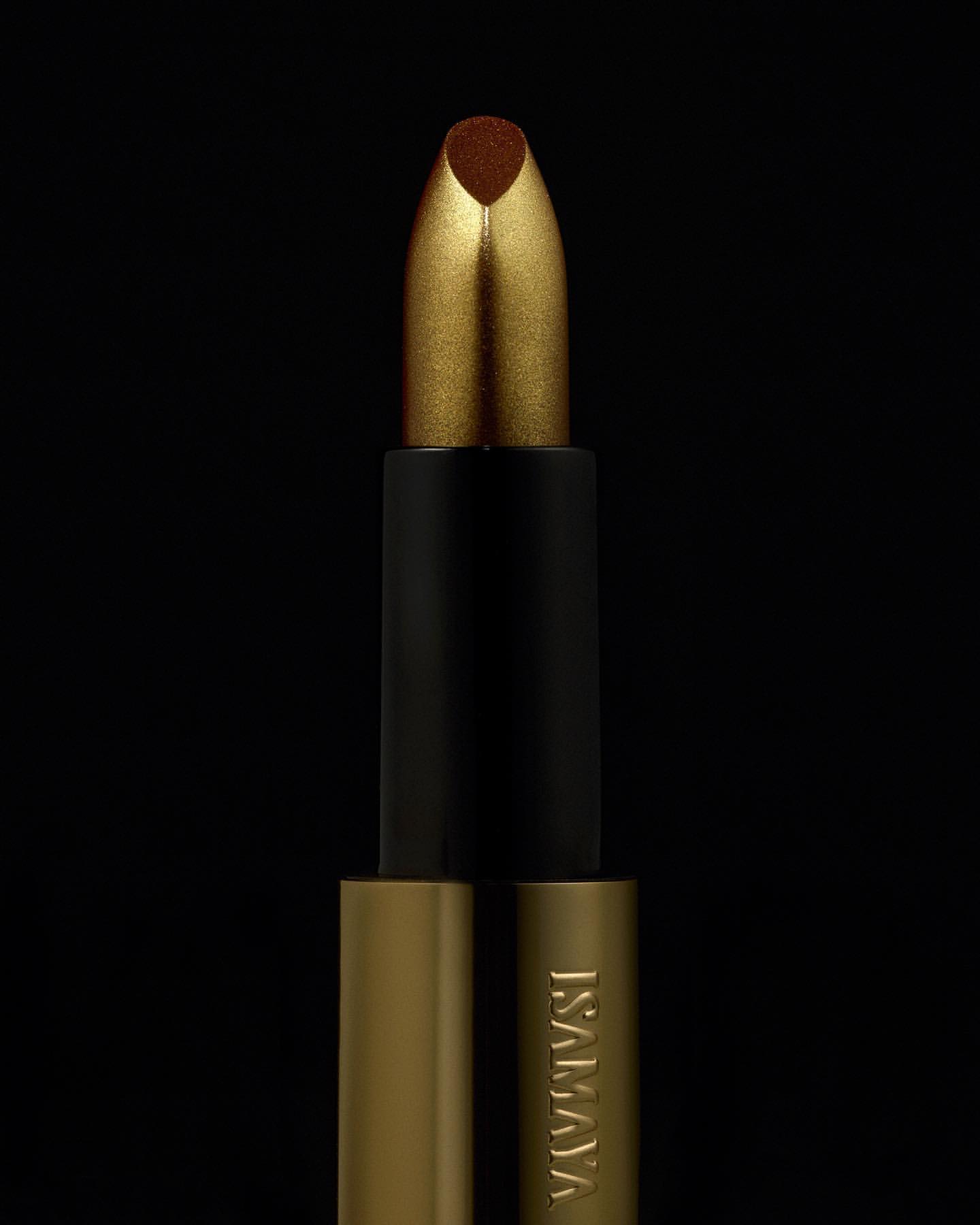 Close-up of gold and black lipstick tube on black background, beauty product advertisement with metallic textures.