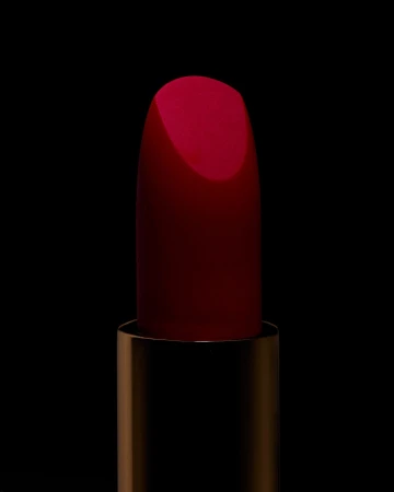 Extreme macro close-up of a crimson red lipstick bullet emerging from its metallic golden case against a pitch-black background.