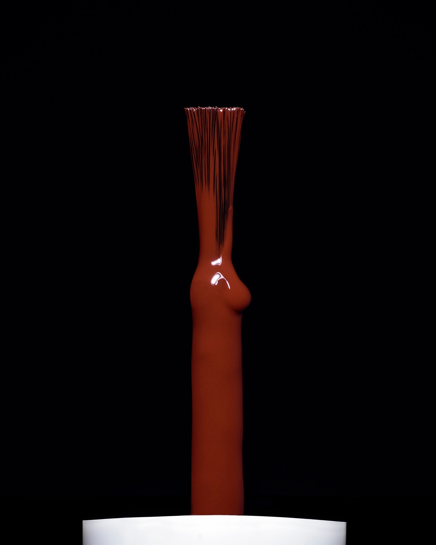 Close-up studio shot of a nail polish brush applicator with terracotta-brown, glossy liquid against a stark black background.