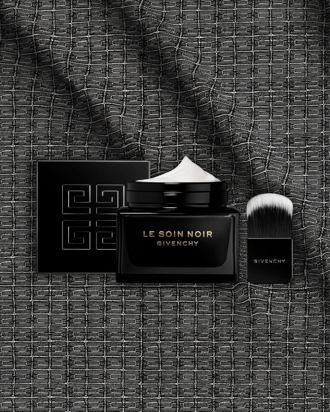 Luxury Givenchy skincare products on a textured dark background. The set includes cream, powder, and a makeup brush for beauty application.