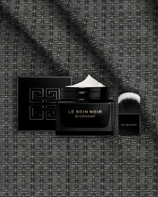 Luxury Givenchy skincare products on a textured dark background. The set includes cream, powder, and a makeup brush for beauty application.