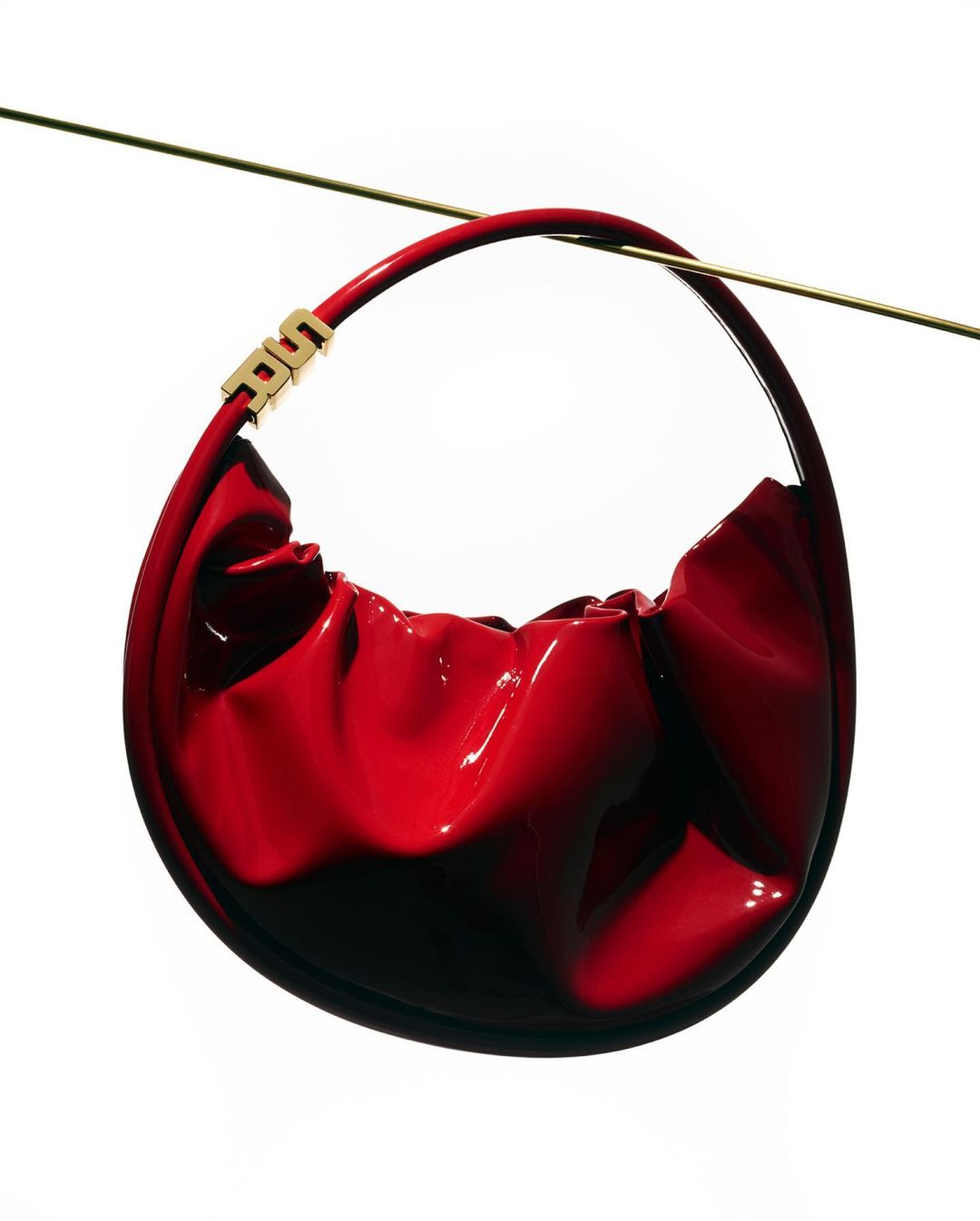 Red patent leather hobo bag with gold accents, suspended by a thin gold wire against a clean white background.