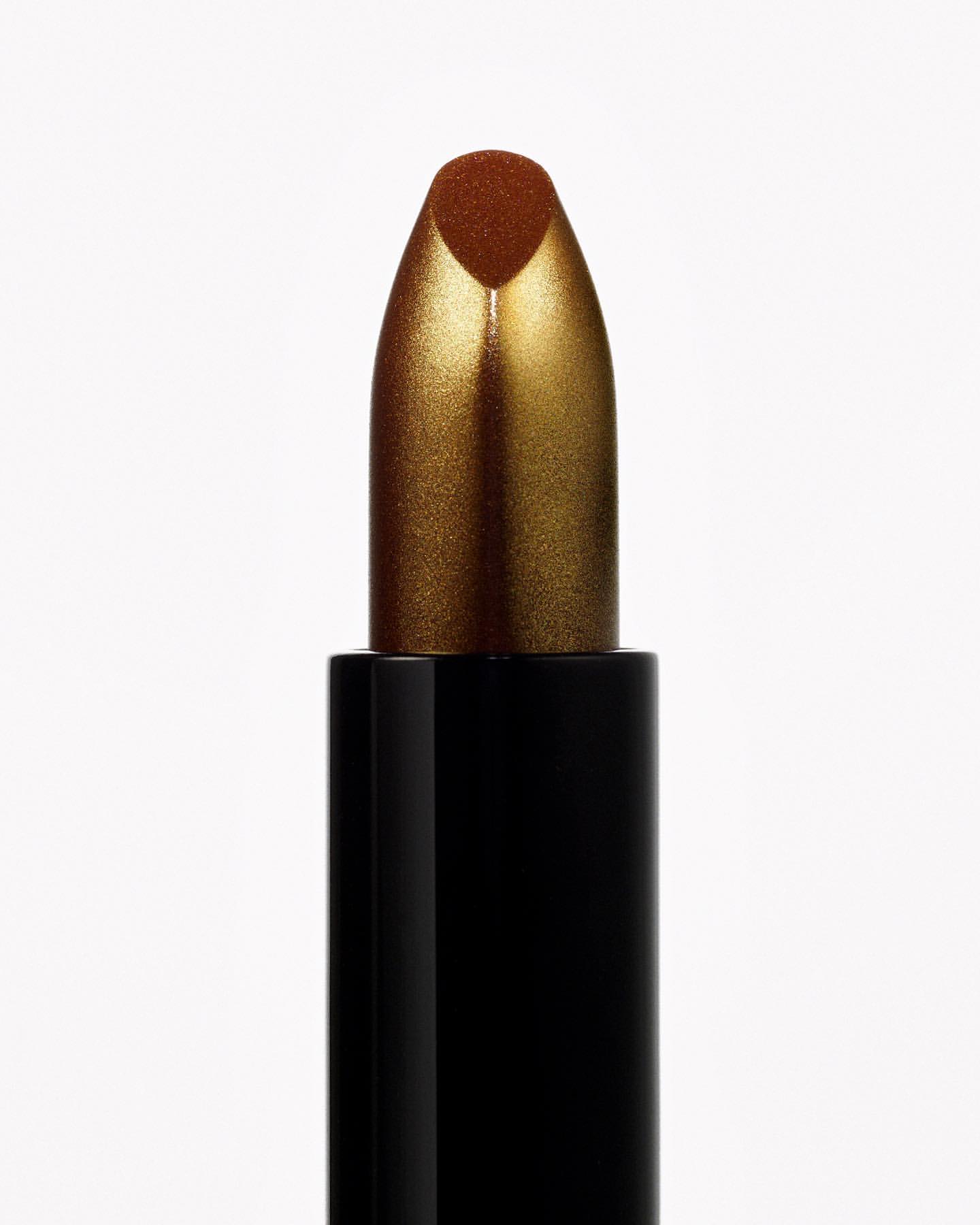 Close-up studio shot of bronze lipstick tube with golden shimmer on a clean white background, emphasizing the product's colors and texture.