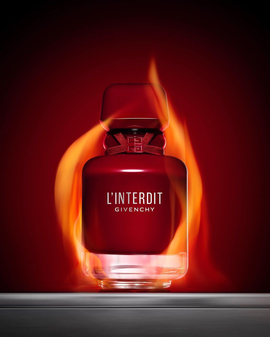 A dark red perfume bottle, L'Interdit by Givenchy, stands centered against a fiery red backdrop, reflecting a hot, luxury aesthetic.