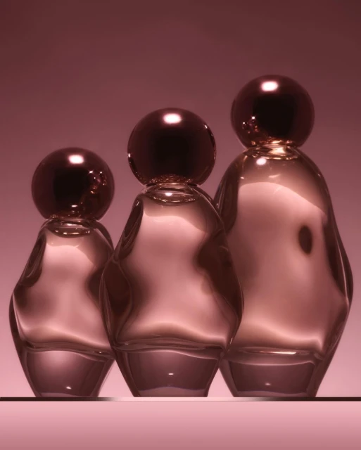 Three glass perfume bottles in varying sizes arranged on a pink surface against a pink backdrop, with light reflecting on their surfaces.