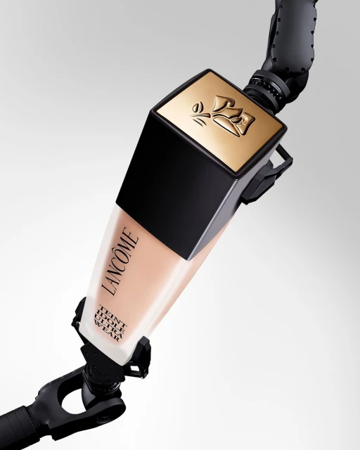 Lancôme Teint Idole Ultra Wear foundation bottle in a light shade, supported by an articulated robotic arm against a white backdrop.