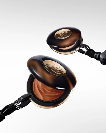 Product shot of two Lancome bronzers. Bronzer compacts are presented open with robotic arms holding them on a white backdrop.