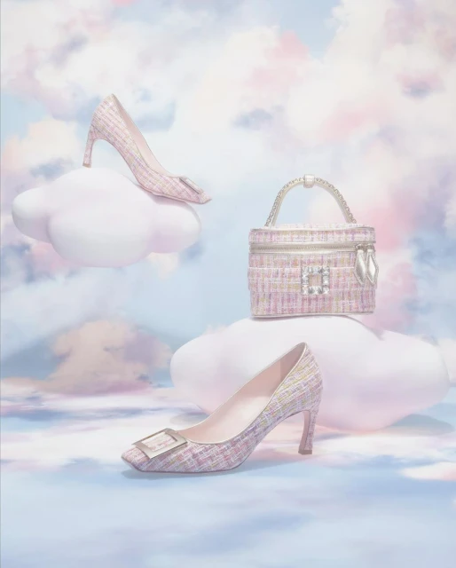 Tweed pumps and a handbag are arranged on white clouds against a sky-like background, presenting a whimsical fashion product display.