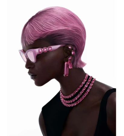 Profile portrait of a Black woman with short pink hair wearing pink crystal sunglasses and layered gemstone necklaces