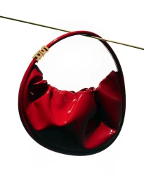 Glossy red handbag hanging over a thin horizontal wire against a white background