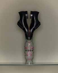 Two black leather dress shoes standing upright inside a stacked green patterned glass vase bound with pink string.