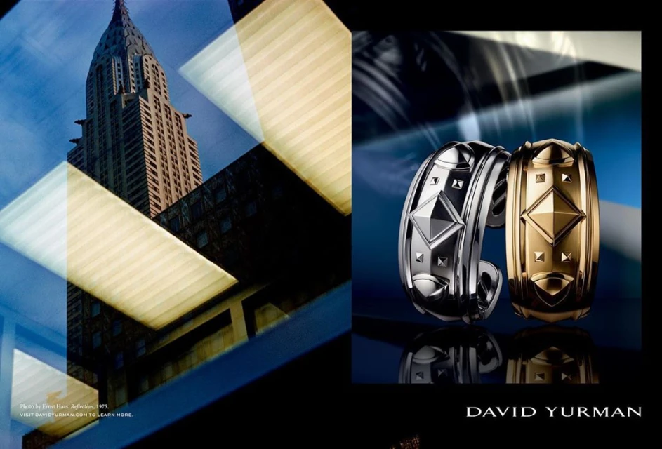 Jewelry ad featuring two designer metal cuff bracelets with a pyramidal stud design, juxtaposed against an urban architectural backdrop.