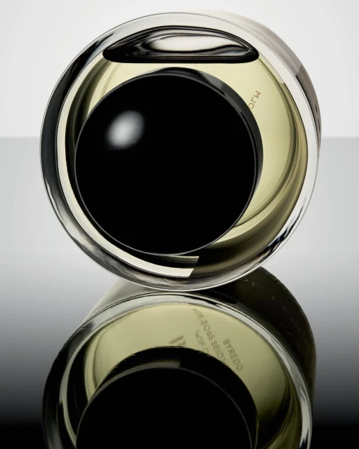 Close-up shot of a reflective, rounded Byredo perfume bottle with a black cap, showcasing its unique design against a gradient backdrop.