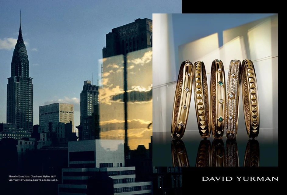 Fashion shot of gold David Yurman bangles with gemstones on a reflective surface, with a city skyline of New York in the background.